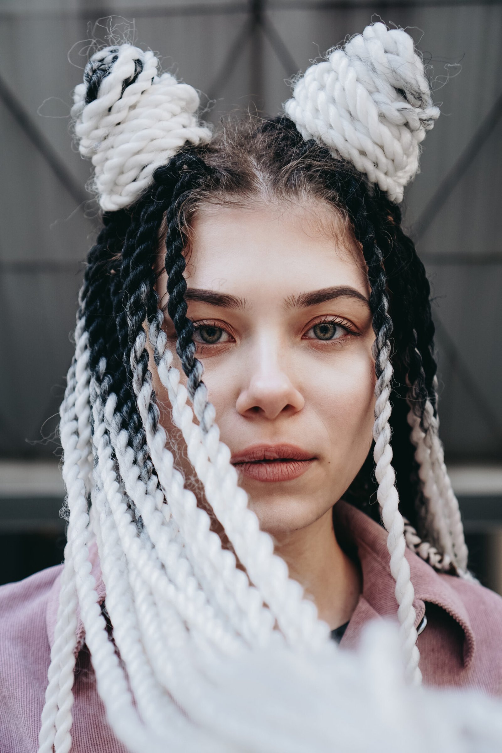 Young woman with futuristic looks. Girl with black and white dreadlocks or pigtails. Against the background of a futuristic building